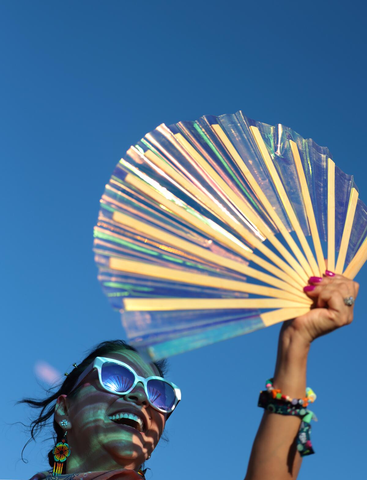 A woman wearing sunglasses holds a fan in front of her face as Teddy Swims performs