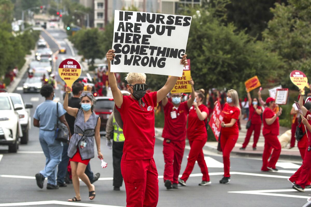 People in red scrubs and wearing masks hold up signs in the middle of a street.