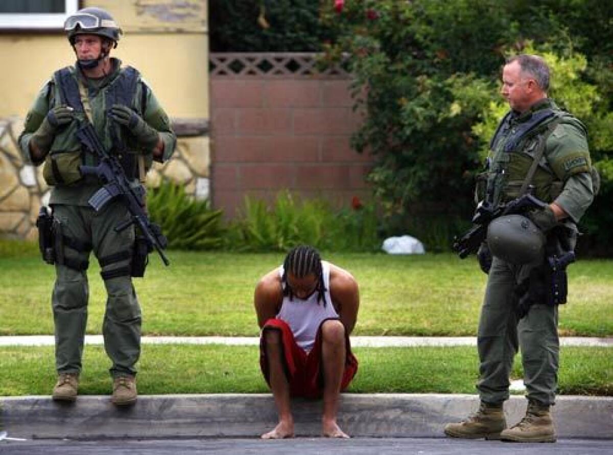 Los Angeles County Sheriff's Deptartment personnel watch over a man detained during a gang sweep conducted to crack down on a violent clique of the Bloods gang, centered in the Compton area.