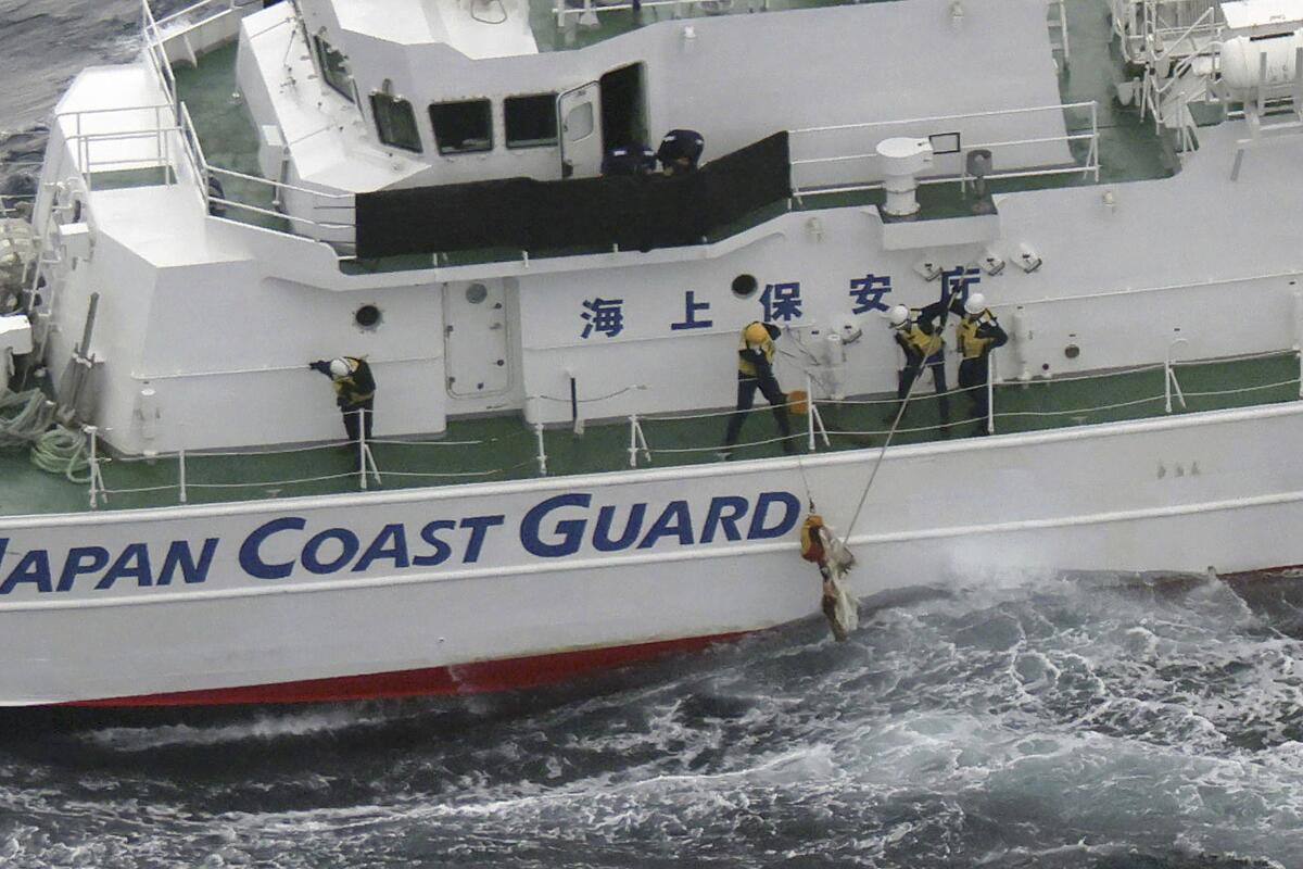 Japanese coast guard members pick up a floating object while conducting a search-and-rescue operation.