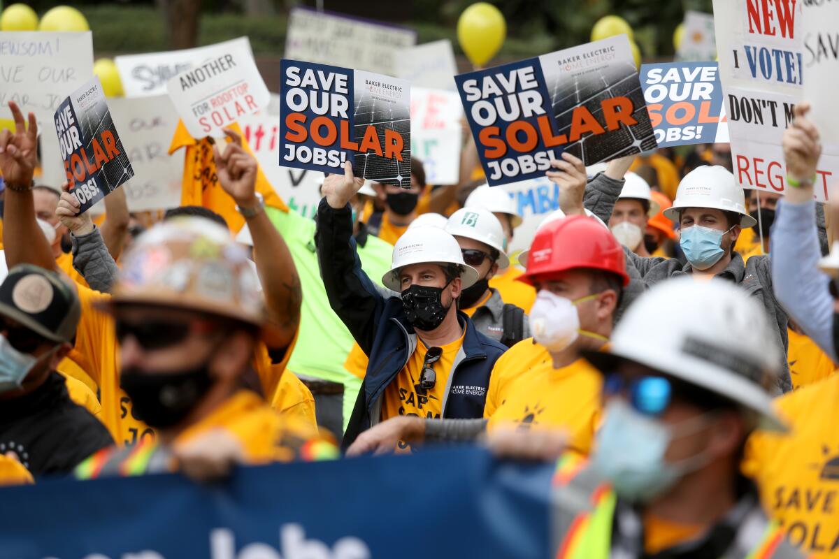 People in face masks, hard hats and yellow T-shirts stand together holding signs that say "Save our solar jobs!"