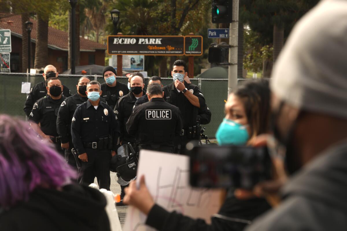  Police and protesters stand outside a fenced Echo Park 