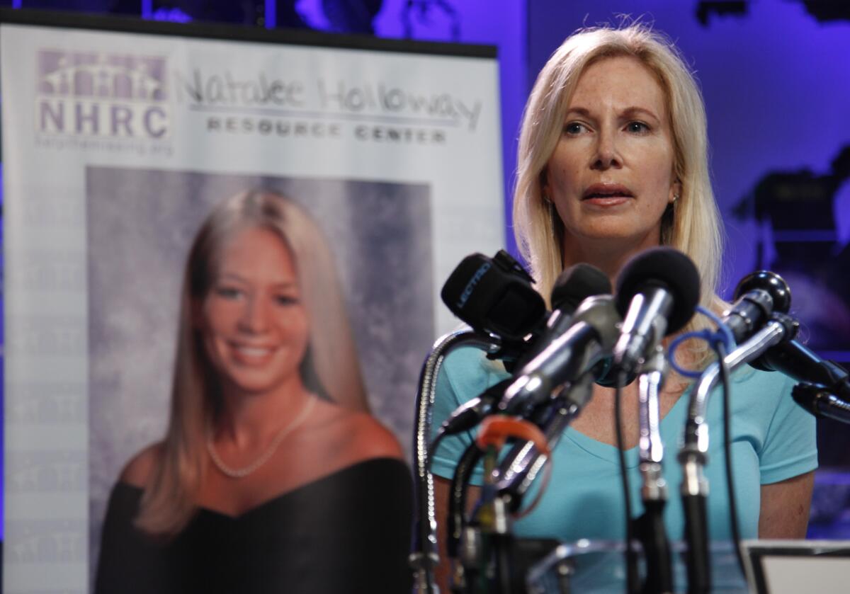 Beth Holloway stands at a microphone in front of a portrait of Natalee Holloway.