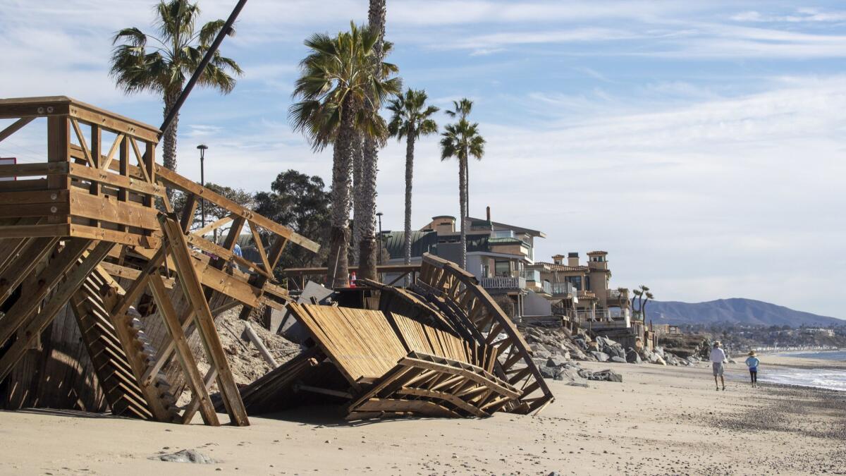 A couple watch Orange County Public Works crews remove a damaged boardwalk at Capistrano Beach in Dana Point.