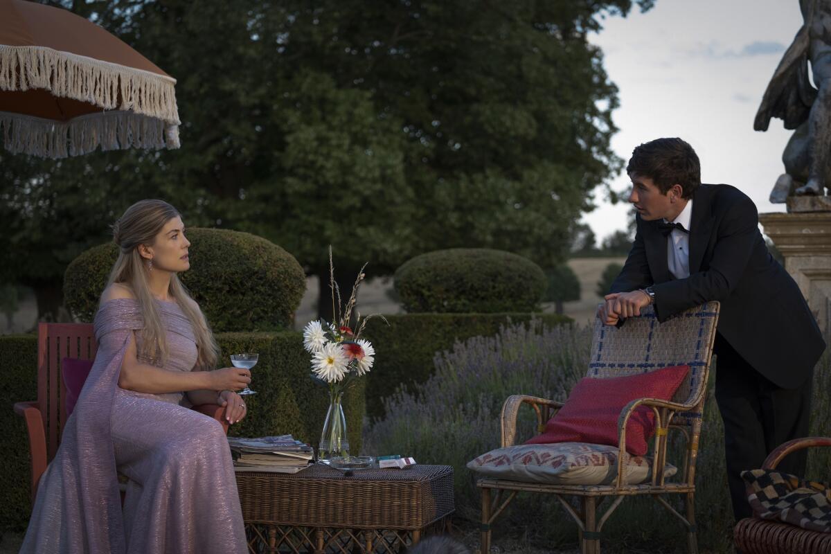 An elegant woman in a purple gown, seated for drinks on the grounds of a country estate, with a young man in a dinner jacket.