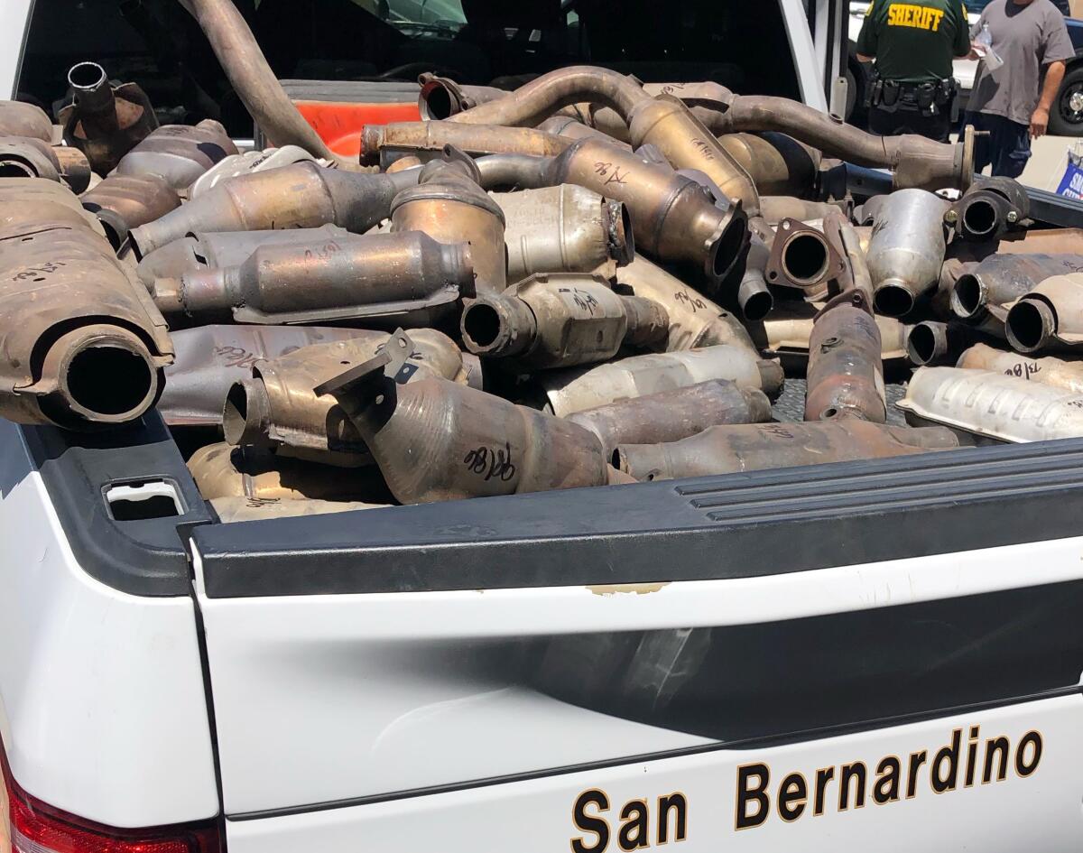 The bed of a white pickup truck brimming with oxidized catalytic converters, some marked with black ink