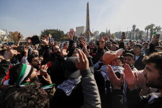 A sea of people, with arms raised, gather in a square