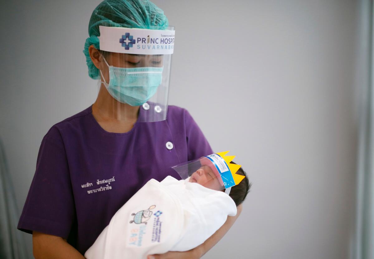 A nurse holds a newborn baby, both wearing face shields