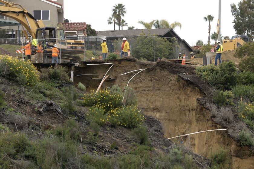 ENCINITAS, CA - MARCH 11, 2023: Workers stand near a large sinkhole that formed from recent rains at the south end of Lake Drive in Cardiff on Saturday, March 11, 2023. (Hayne Palmour IV / For The San Diego Union-Tribune)