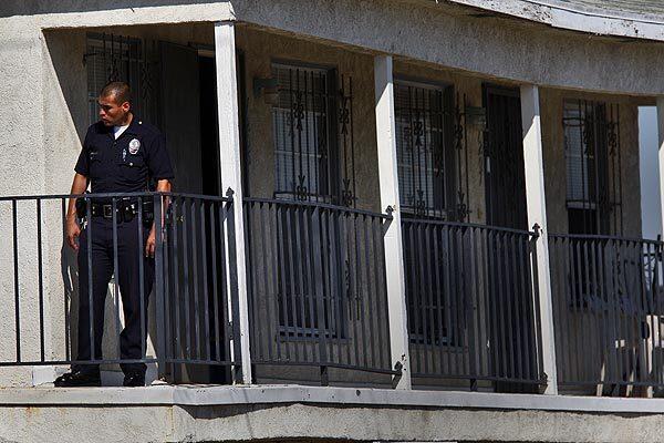 An LAPD officer stands on the balcony of an apartment complex where a mother was arrested after 5-year-old boy was found shot dead and his brother injured in South Los Angeles today. The complex is in the 7200 block of South Gramercy Place.