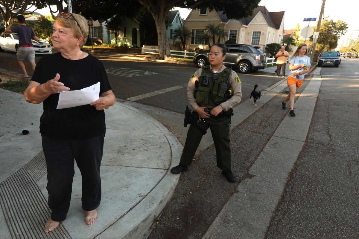 A person stands barefoot on a street as a law enforcement officer watches them.