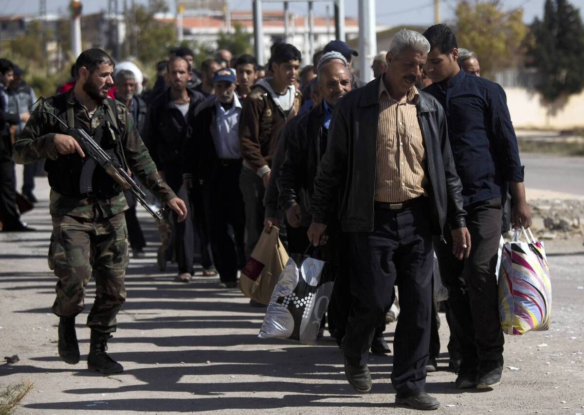 A Syrian soldier escorts men arriving from the rebel-held suburb of Muadhamiya to Damascus. The suburb, which is under government siege, has been cut off from food and medicines for months.