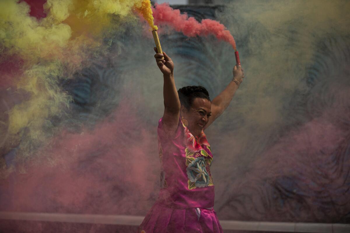 A person holds up two tubes that emit colorful smoke.