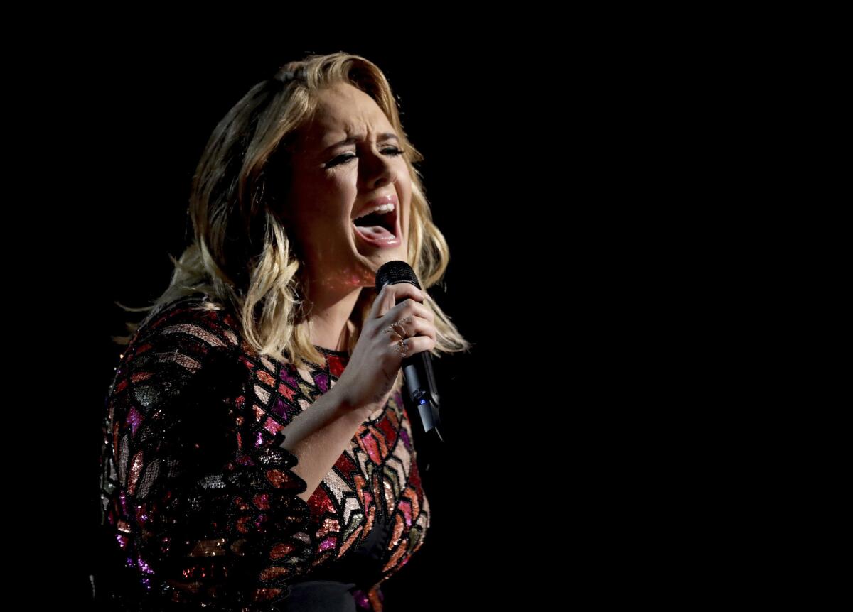 A blond woman in a sequined dress of many colors singing into a microphone