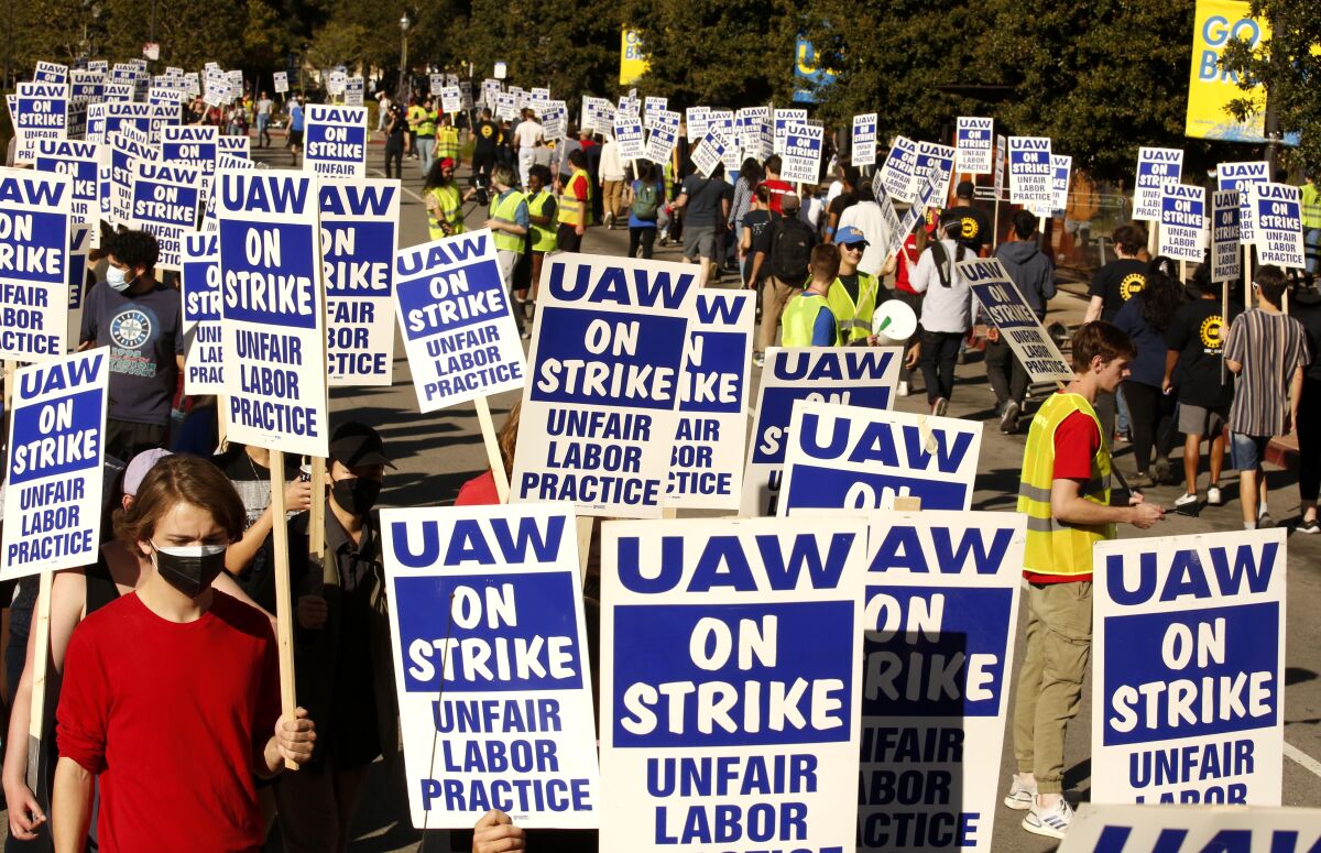 Dozens and dozens of signs are seen as protesters march outdoors. The signs say "UAW on strike: Unfair labor practice."