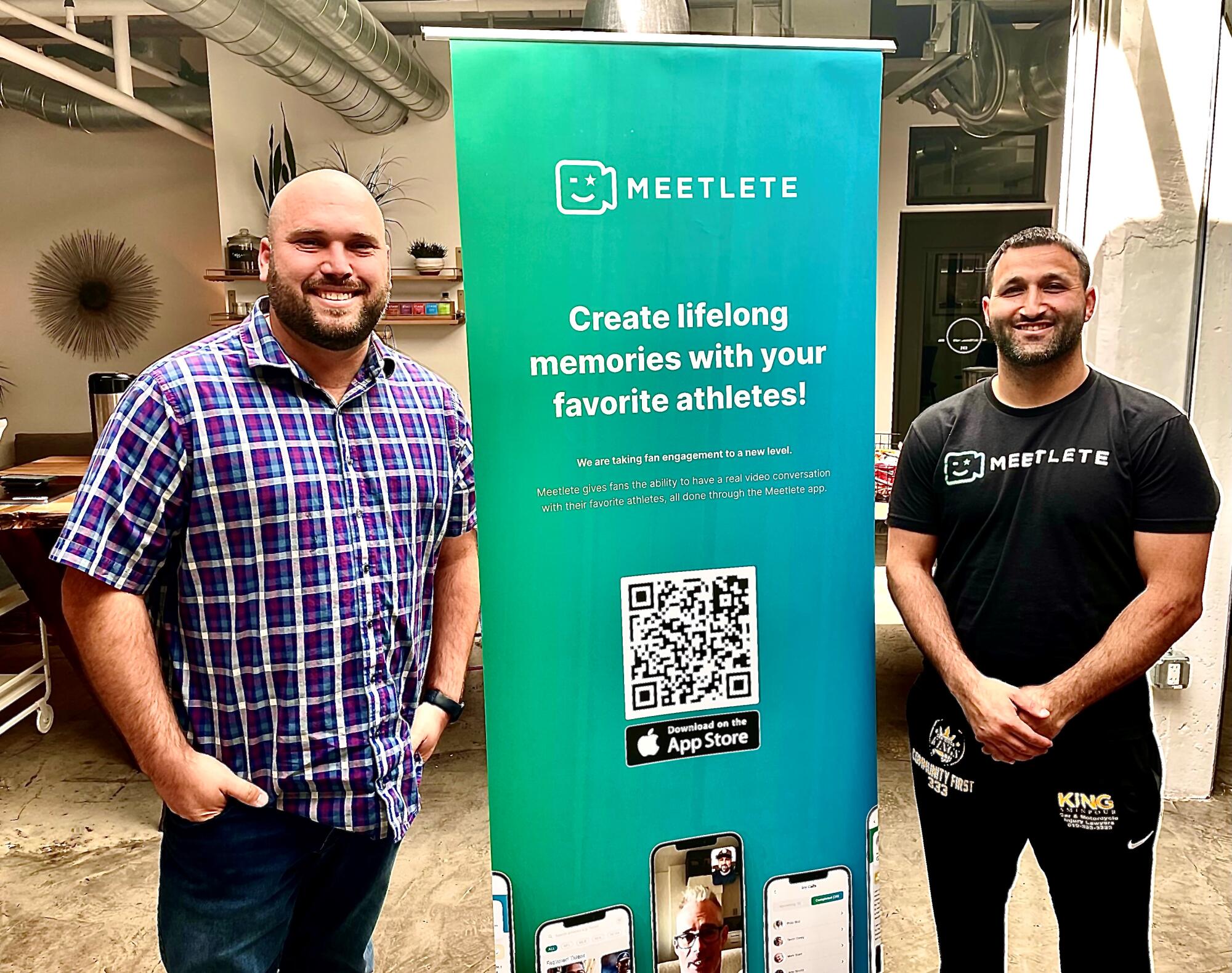 Two men stand next to a sign for Meetlete, a sister company of Finlete. 