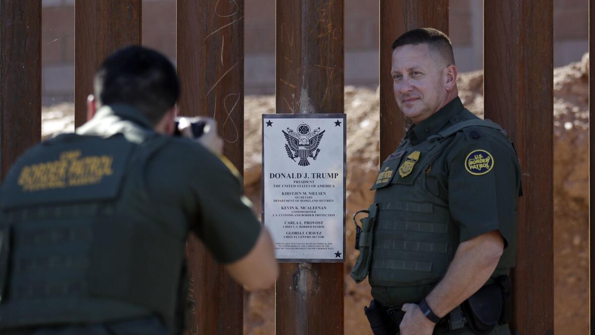 Border Patrol agent Michael Sullivan poses for a picture next to a plaque adorning a newly fortified border fence in Calexico, Calif.