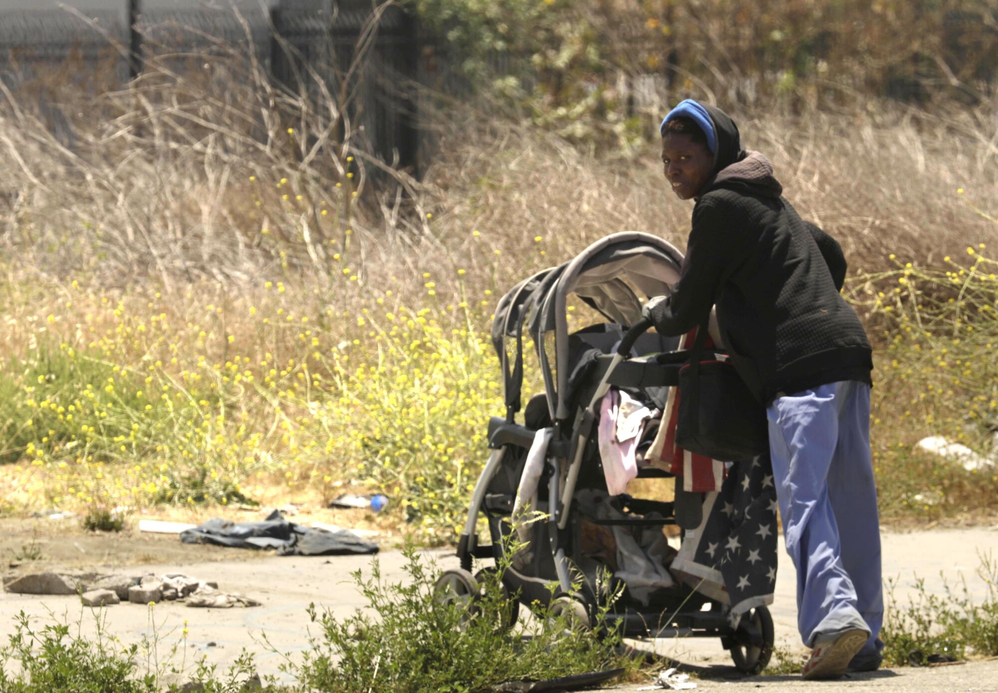 A homeless woman pushes a baby stroller filled with her belongings through a 10-acre vacant lot in Watts.