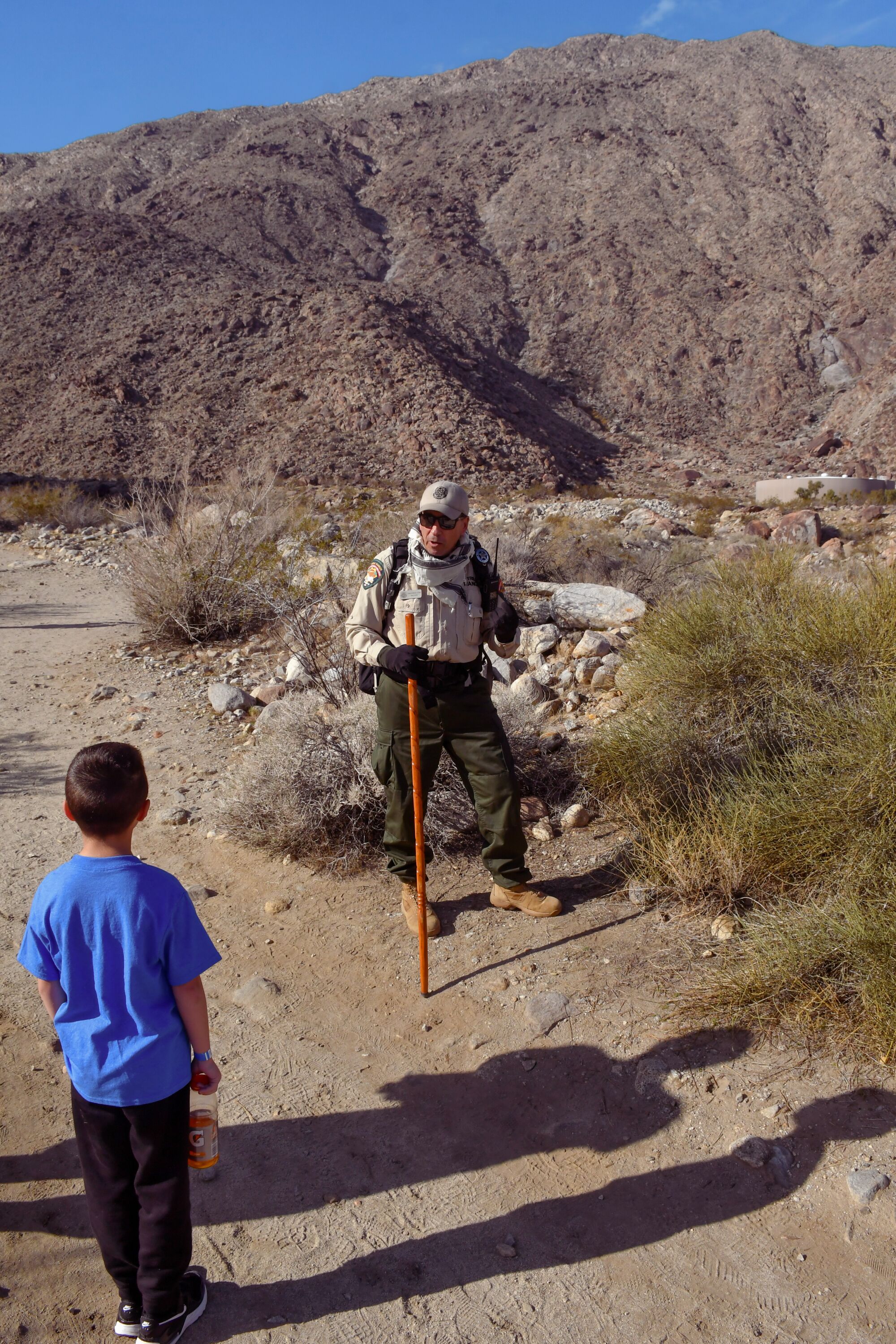A ranger stands on a trail talking to a young boy.