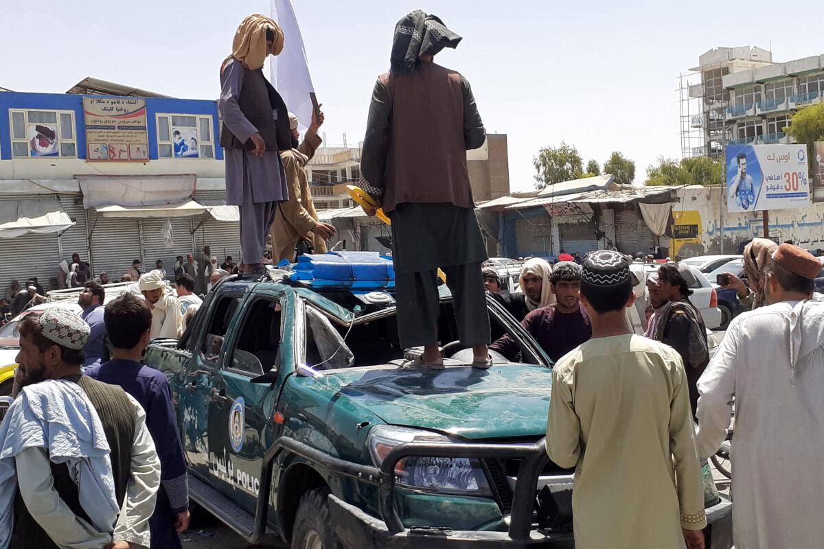 Taliban fighters stand over a damaged police vehicle Friday in Kandahar.