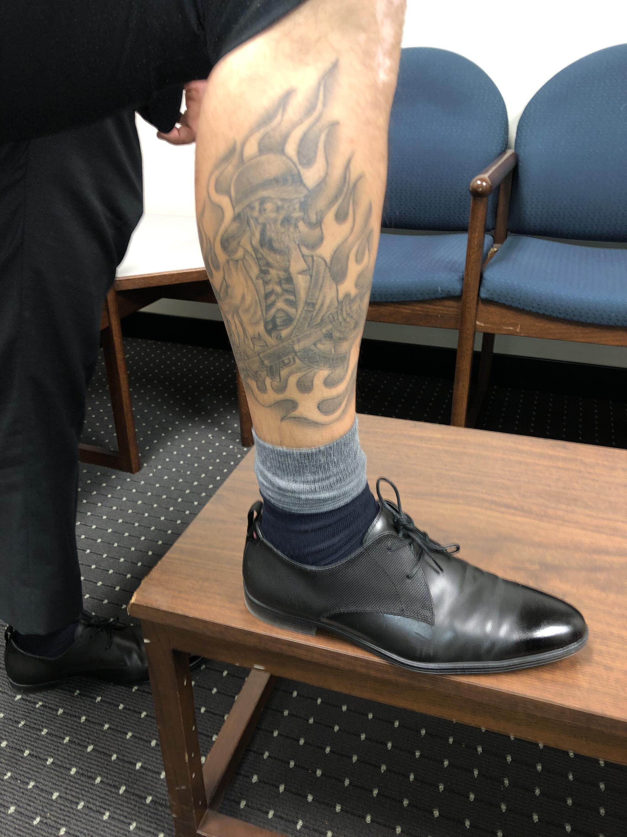 A tattoo of a skull with a rifle and a military-style helmet surrounded by flames on the right leg of a sheriff’s deputy