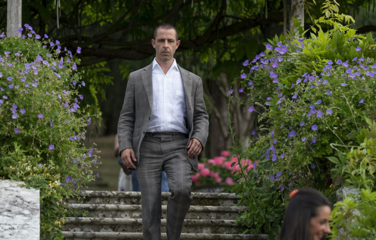A man in a suit walks down stairs amid blooming flowers.