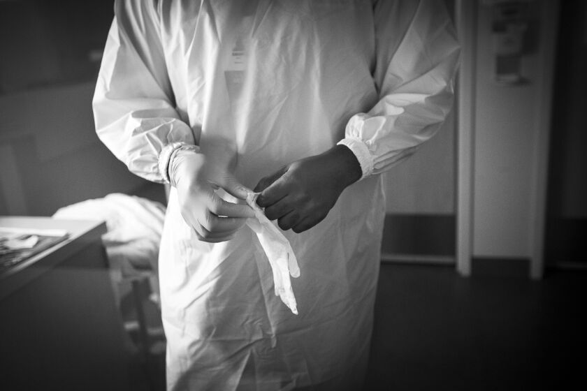 LOS ANGELES, CA - APRIL 27: (Editor's note: Image for story by Francine Orr and not for generic use at this time. Mary Cooney/ photo editor) Patient Care Technician Rakeem Addison, (CQ), age 30, puts on his white gloves and his isolation gown before entering into a covid-19 patient's room at Martin Luther King, Jr., Community Hospital on Thursday, April 27, 2020 in the Willowbrook neighborhood located in South Los Angeles, CA. He is currently working on the COVID-19 Unit at MLKCH. He said he was homeless from about age 15 to age 25 years old. He said he got fed up being homeless and started surrounding himself with successful and wanted to a part of the healthcare system. He started as a volunteer. He said as a homeless person he would stay at friend's homes and then inside his car until it was towed. He also said he used to stay on the path near King Drew High School. He went to high school in Long Beach where he played basketball. He says his father was from West Africa, in Accra, Ghana. He says his family now says he is strong. He says this November it will be his forth year working here. (Francine Orr / Los Angeles Times)