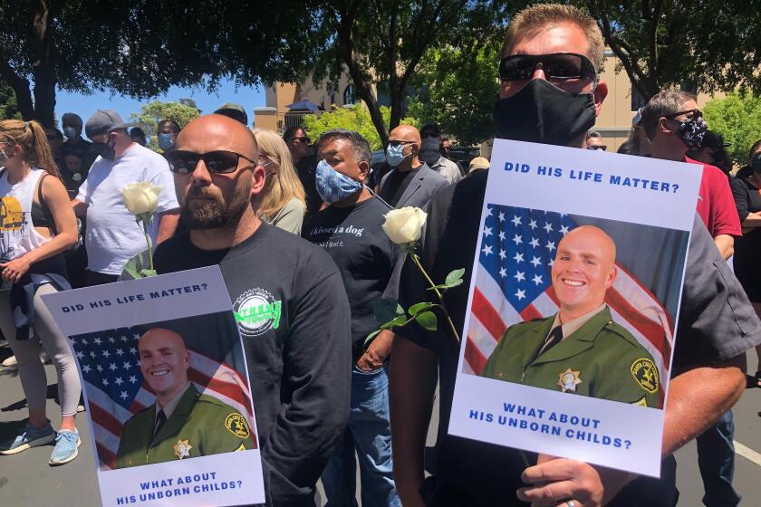 Matthew Rose, left, and Michael Carr, of Santa Cruz County hold posters of slain Sgt. Damon Gutzwiller, as they join others outside the Santa Cruz County Sheriff-Coroner's Office to pay their respects in Santa Cruz, Calif., Sunday, June 7, 2020. Santa Cruz County Sheriff's Sgt. Gutzwiller, 38, was shot and killed in Ben Lomond, an unincorporated area near Santa Cruz. Sheriff Jim Hart said the suspect, Steven Carrillo, was shot during the arrest and is being treated at a hospital. (AP Photo/Martha Mendoza)