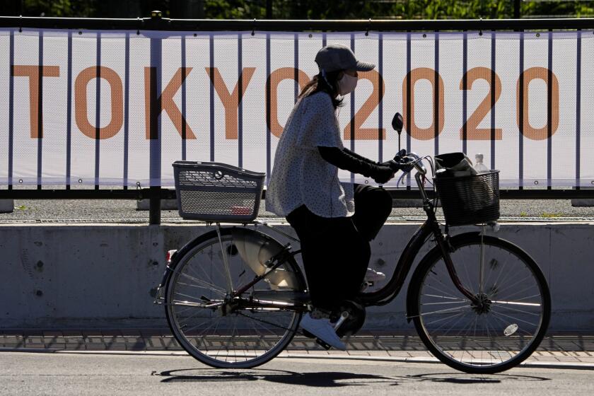A woman rides her bike past signage for the 2020 Summer Olympics outside of Yumenoshima Park Archery Field, Sunday, July 18, 2021, in Tokyo. (AP Photo/Charlie Riedel)