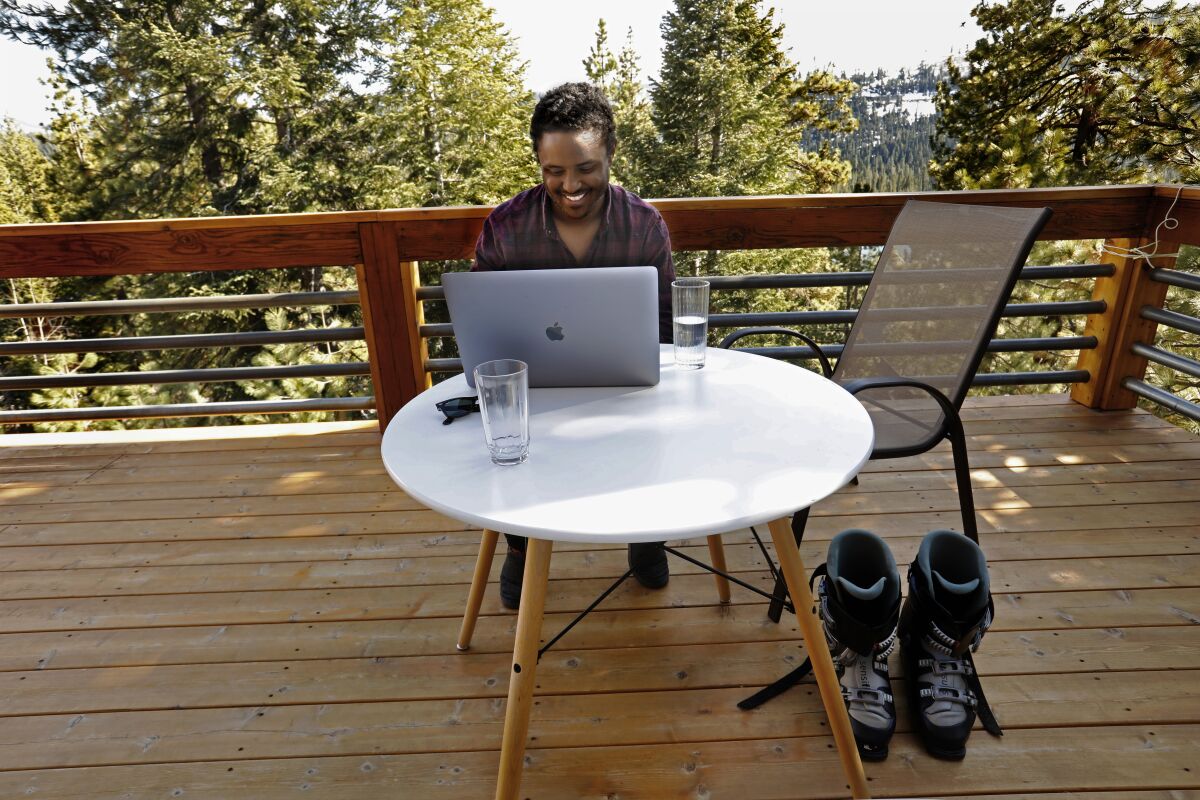 A man works at a laptop on a deck in a forest
