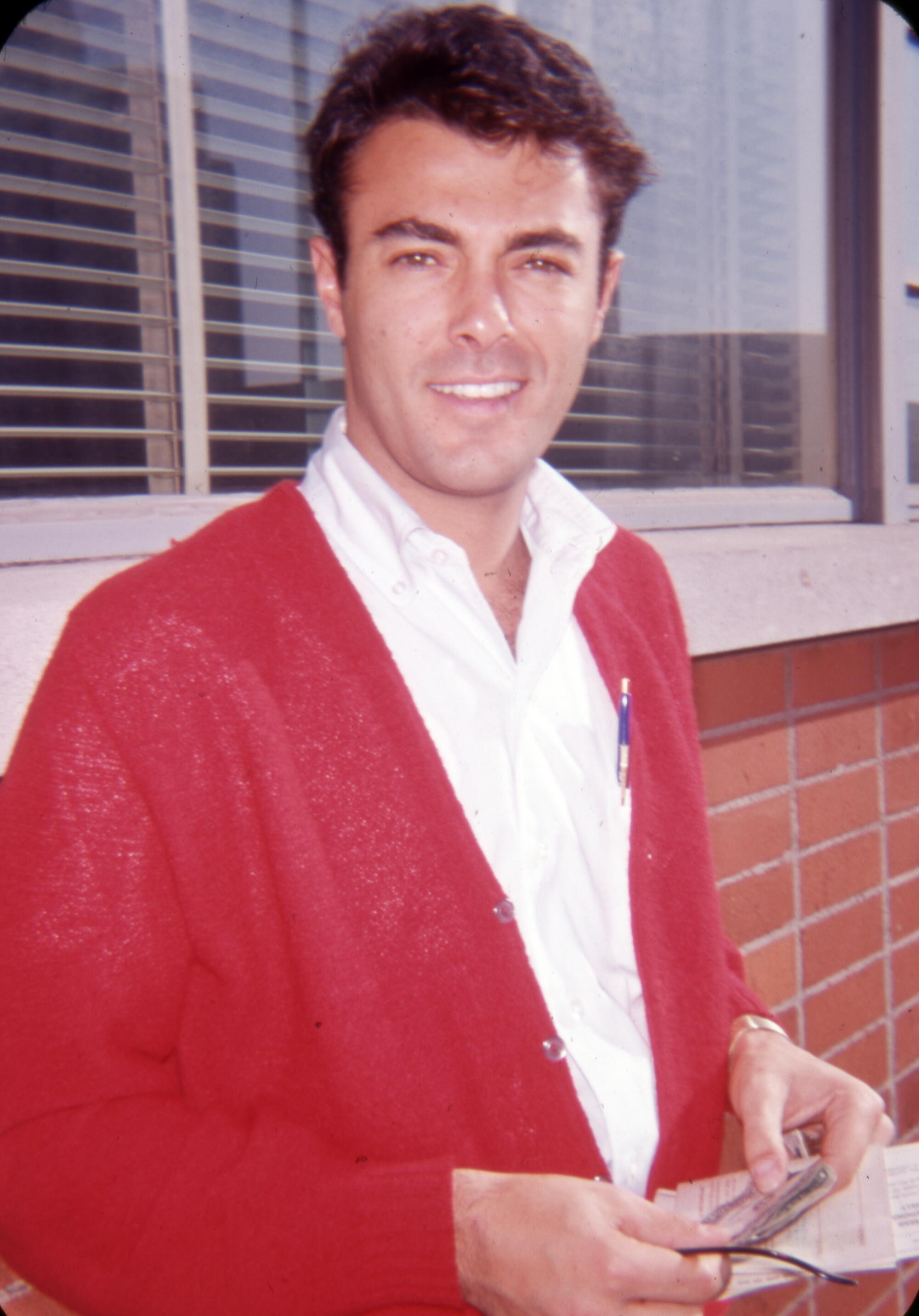A man in a red jacket open at the front smiles toward the camera