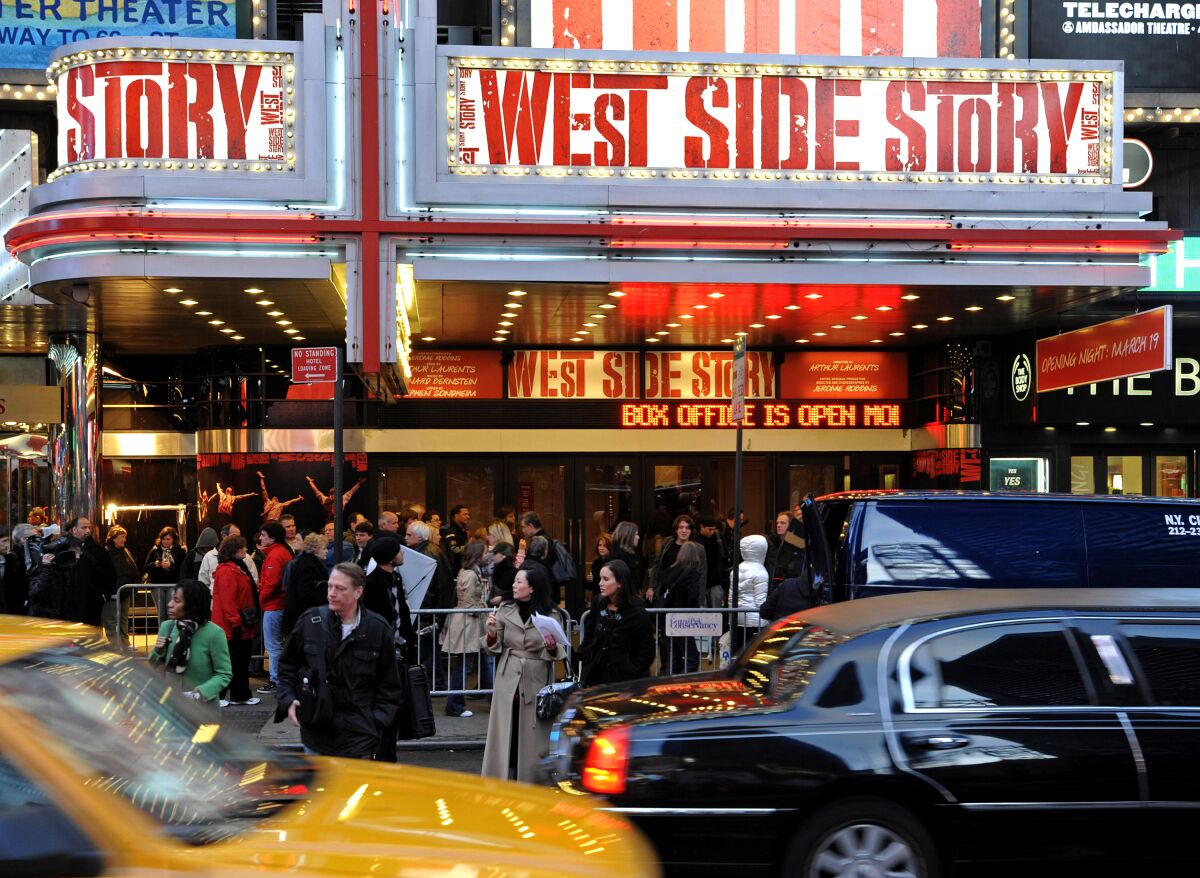 A theater marquee reads "West Side Story" above a sidewalk crowd as New York traffic passes