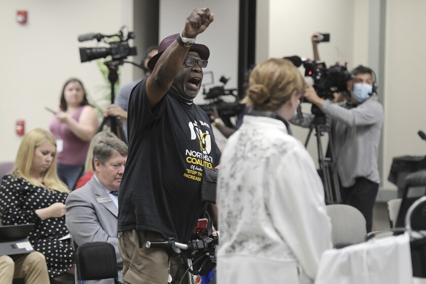 A man stands with a raised fist at a school board meeting among other audience members. 