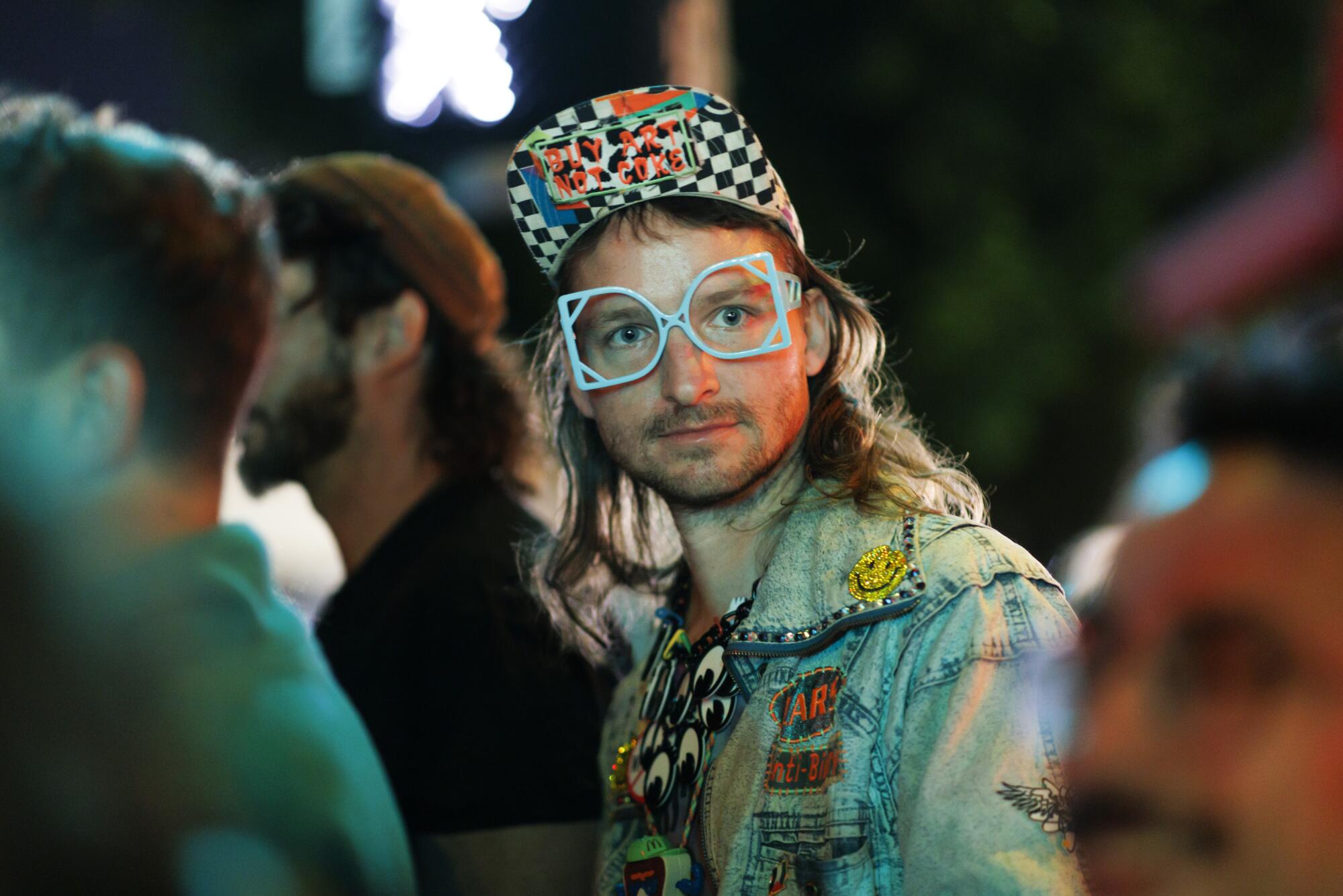 A man in glasses, a checked cap and washed denim jacket with swatches.