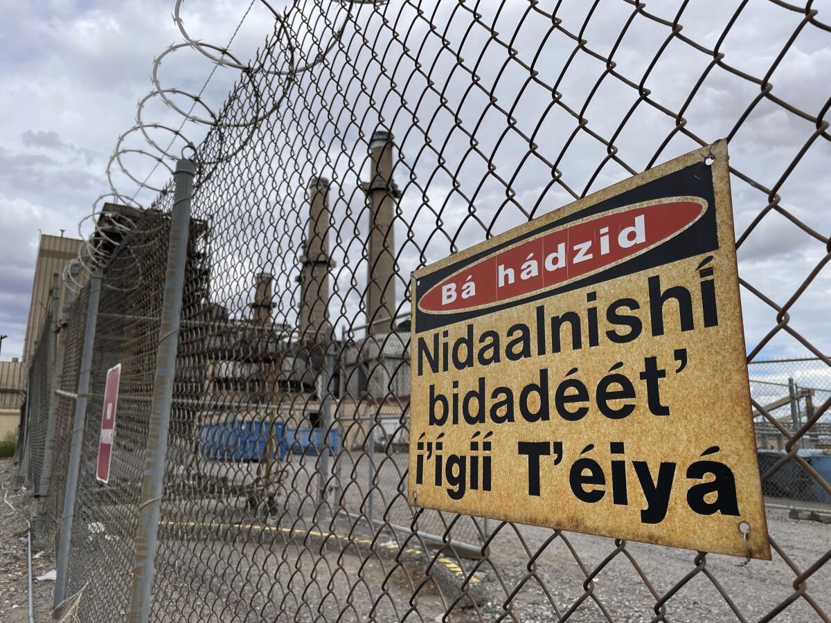 This Sept. 20, 2022 image shows a sign in Navajo on the fence surrounding the San Juan Generating Station near Waterflow, New Mexico. The closure of the coal-fired power plant and the adjacent mine is resulting in the loss of hundreds of jobs and tens of millions of dollars in tax revenue for a local school district that serves mostly Native American students. (AP Photo/Susan Montoya Bryan)