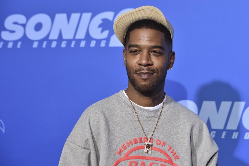 A man posing in a gray sweatshirt and beige hat