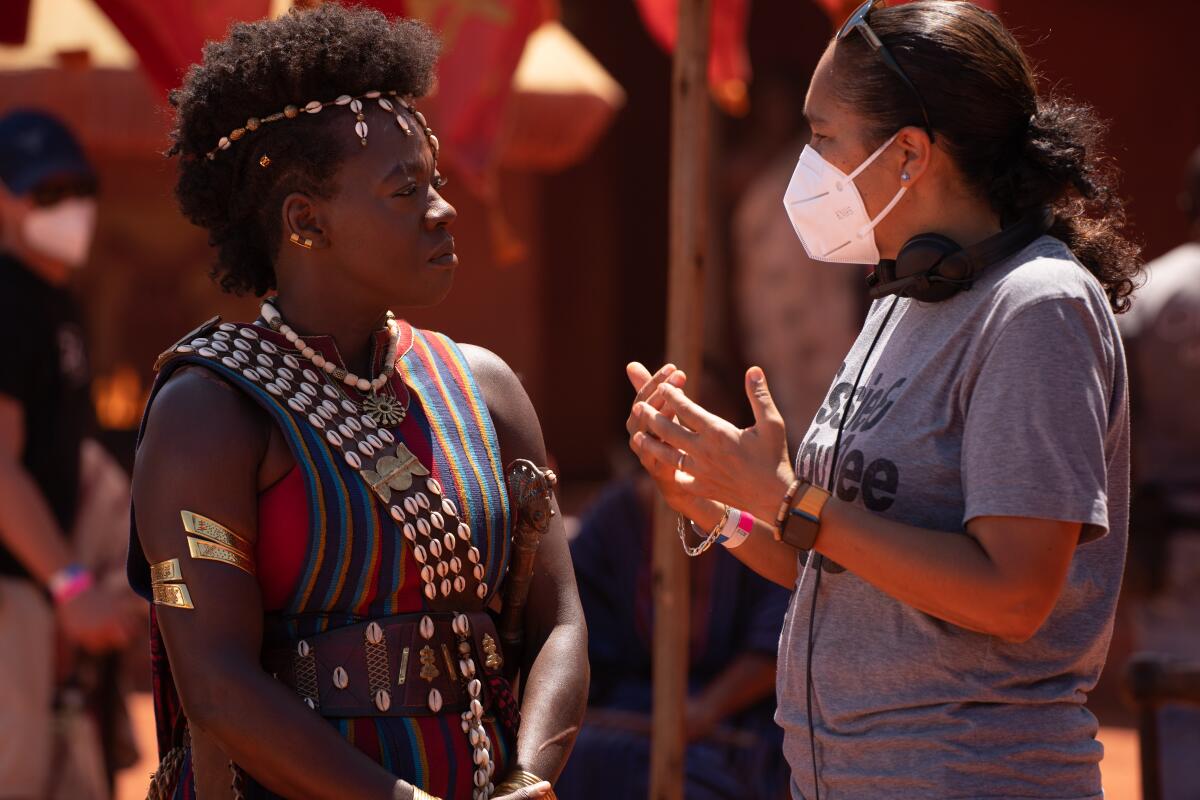 An actress in costume and a director in a T-shirt and face mask talk on a movie set.