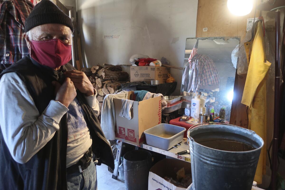 Raymond Clark stands in front of his makeshift washing station in his home in Teesto, Arizona, on the Navajo Nation on Thursday, Feb. 11, 2021. Teesto workers, health representatives, volunteers and neighbors keep close tabs on another to ensure the most vulnerable citizens get the help they need. (AP Photo/Felicia Fonseca)