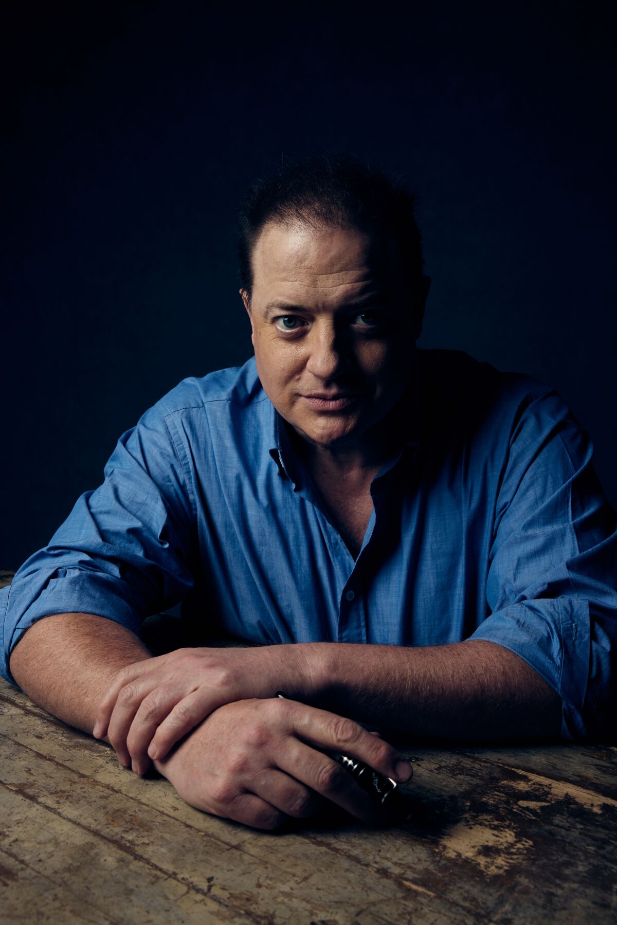 Brendan Fraser leans his arms on a table for a portrait.