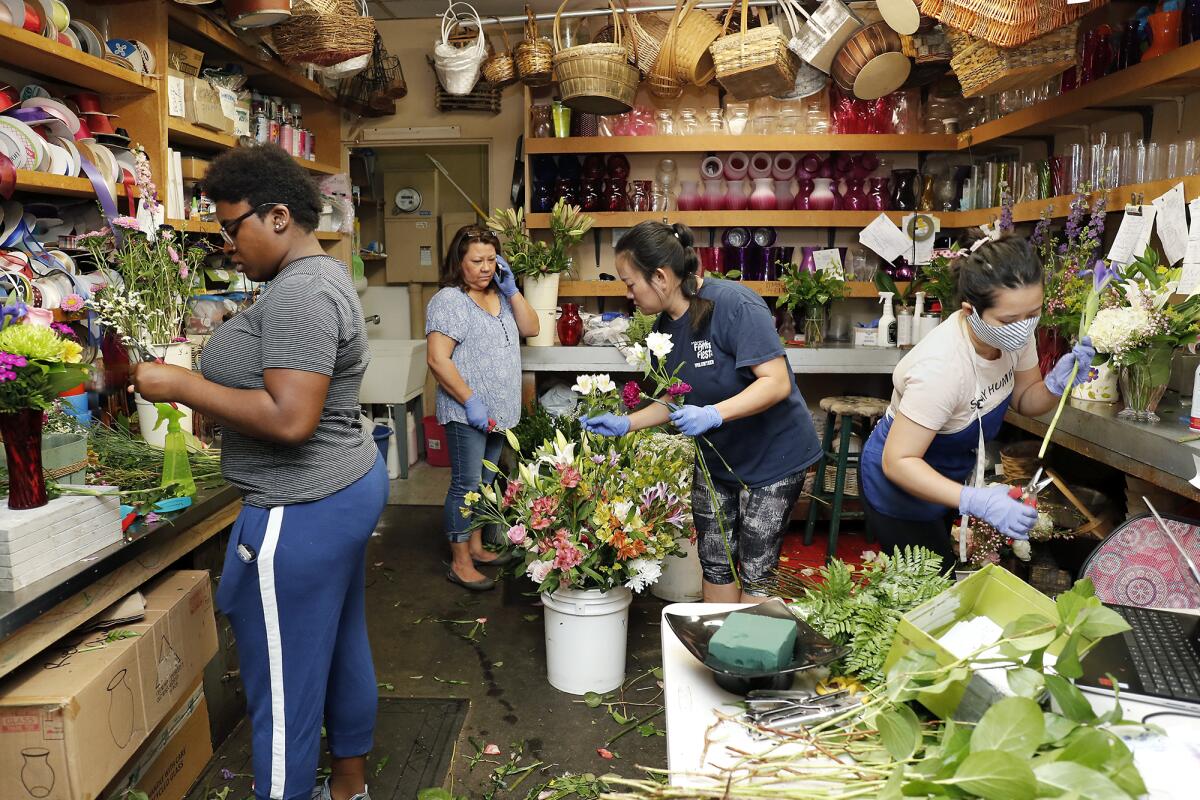 Owner Marcy Horgan, second to left, takes a call as Brittany Cain, far left, Cece Vo, second from right, and Kelly Pham, work to fill orders at Magnolia Florist in Fountain Valley on Friday.