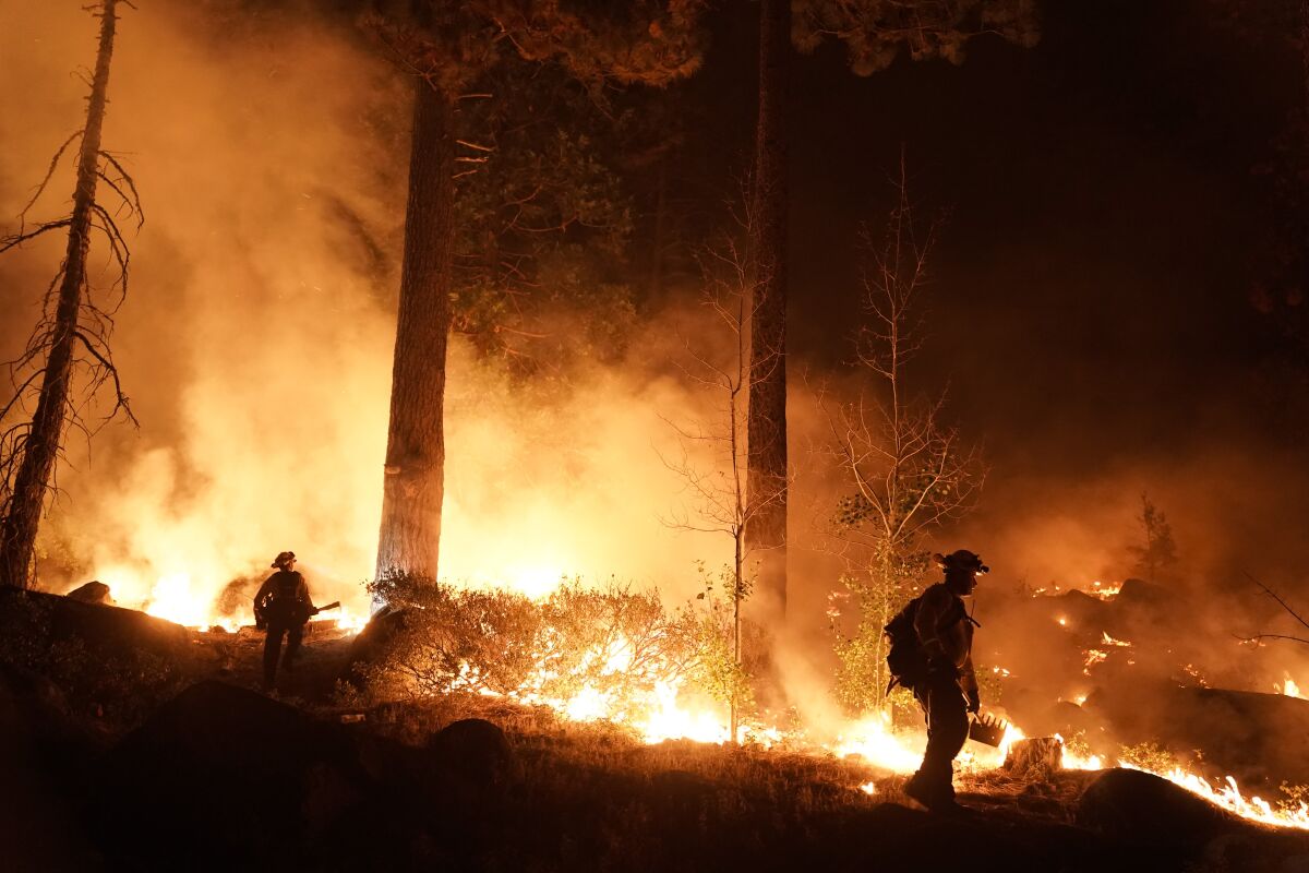 Two firefighters are silhouetted by flames in a burning forest