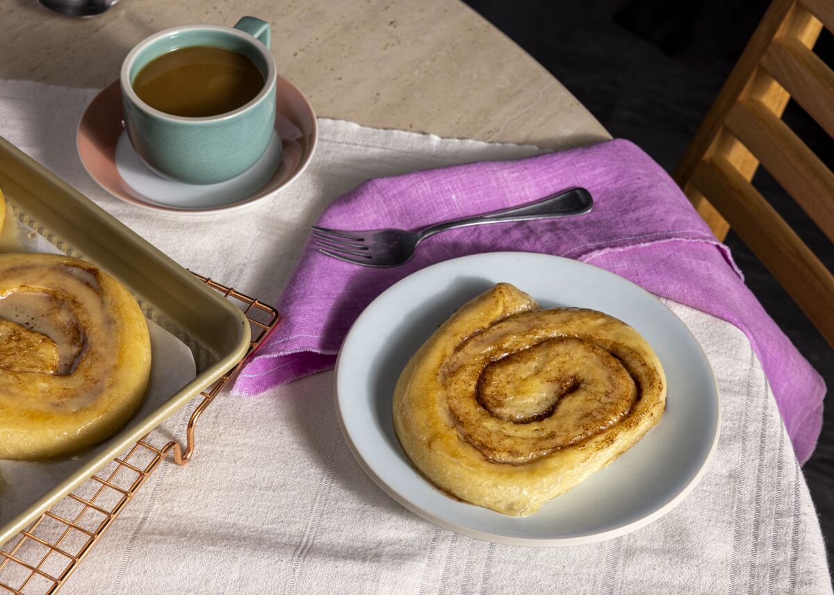 Homemade honey buns on a white plate with a cup of coffee nearby.