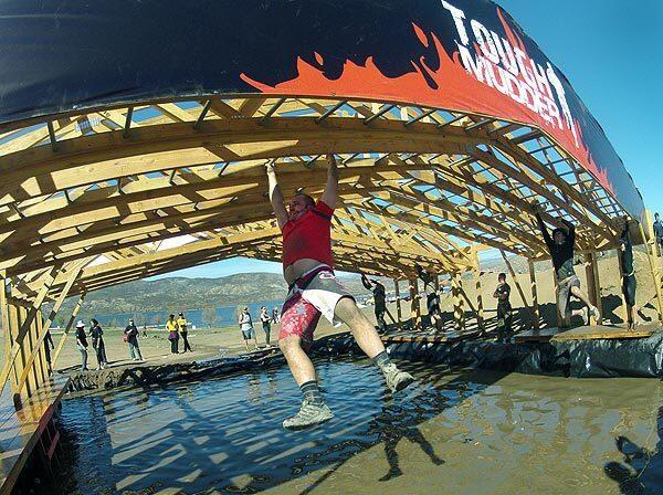 Tough Mudder runners make their way across slicked monkey bars over cold water in the hills near Temecula.