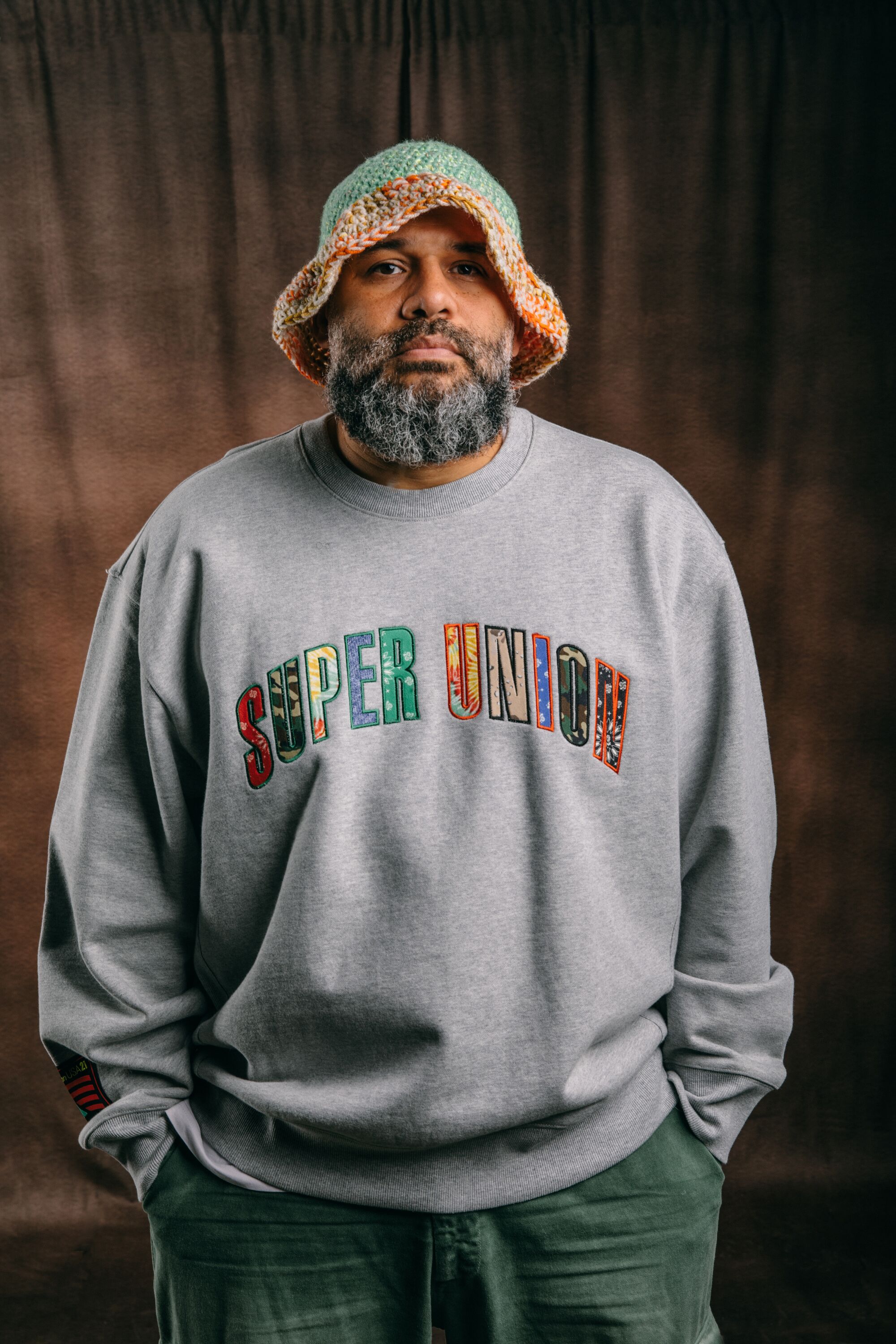a bearded model wearing a Union X Supervsn grey sweater with the words "Super Union" across the front