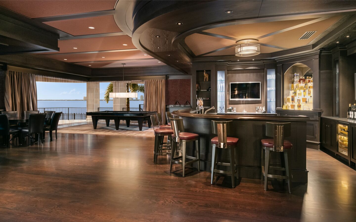The bar has stools, dark colors and an expanse of wood floor.