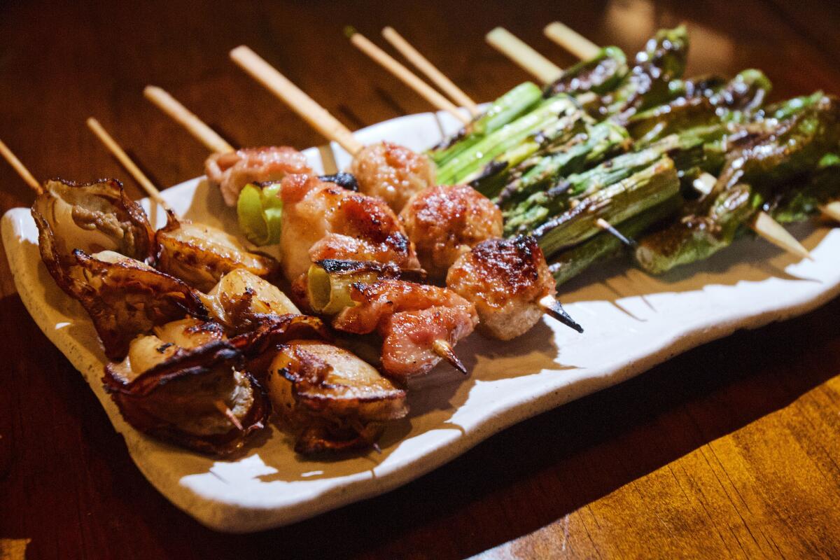 A plate holds stacks of Izakaya Bizan yakitori skewers: scallops, chicken thigh, tsukune, asparagus and shishito peppers.
