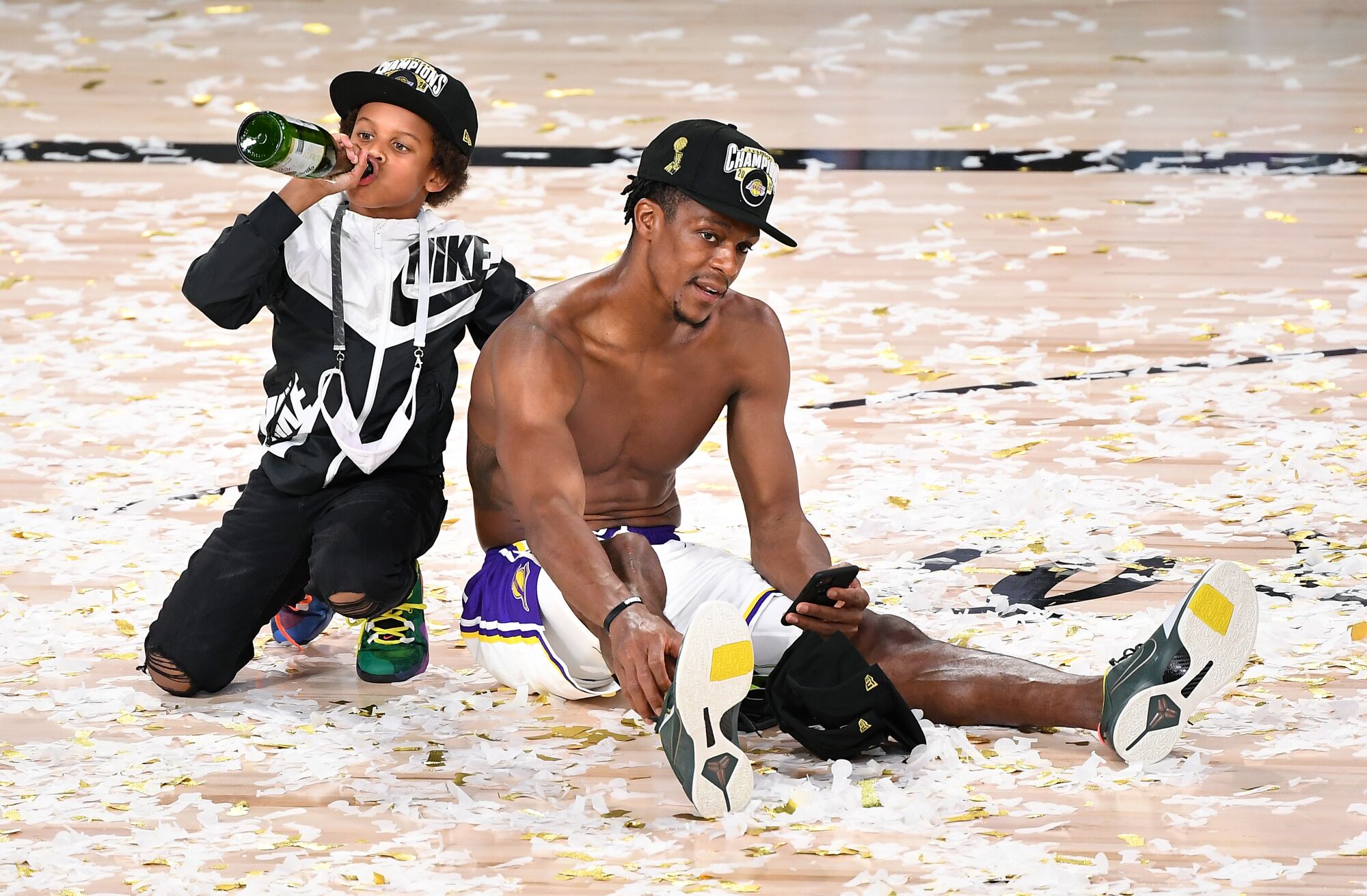 Rajon Rondo relaxes on the court after the NBA Championship as his son Rajon Jr. drinks from a Martinelli's bottle.