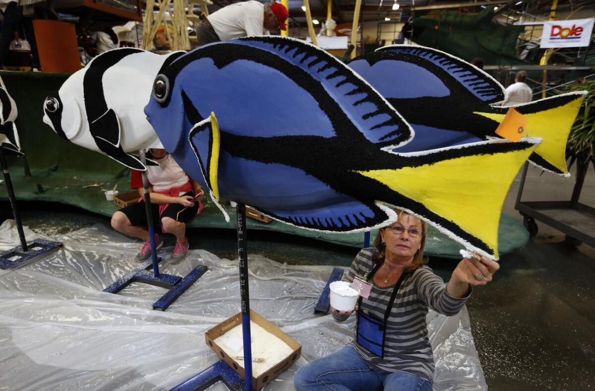 Volunteer Kathi Smith uses glue to apply crushed white rice onto a blue tang fish for a float sponsored by the Lucy Pet Foundation under construction at Fiesta Parade Floats in Irwindale.