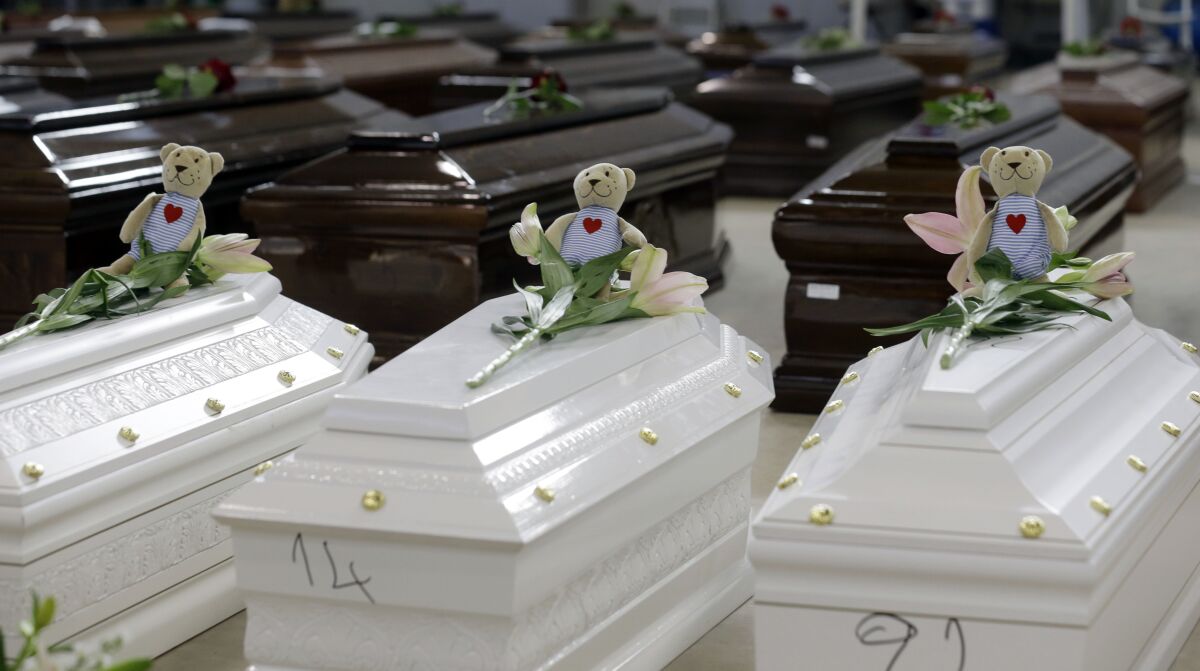 FILE - Teddy bears and flowers placed are placed on the coffins of deceased migrants inside a hangar at Lampedusa's airport, Italy, Saturday, Oct. 5, 2013. A decade ago this year, the head of the EU's executive branch, Jose Manuel Barroso stood visibly shaken before hundreds of coffins holding the corpses of migrants drowned off the Italian Island of Lampedusa. (AP Photo/Luca Bruno, File)