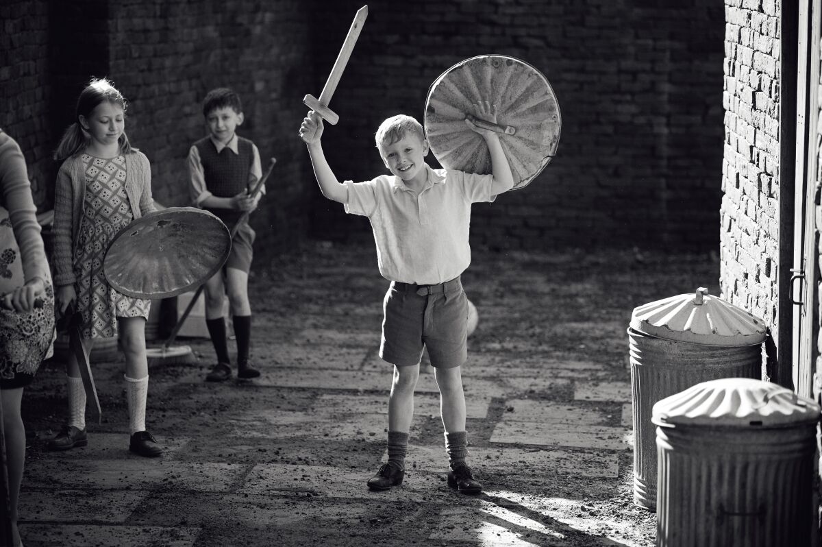 A boy plays soldier with a wooden sword and a trashcan-lid shield in a scene from "Belfast."